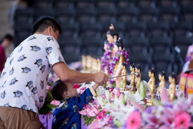 Dibantu orang tua, seorang anak menuangkan air pada rupaka Bayi Siddhatha dalam festival Vesak 2017.